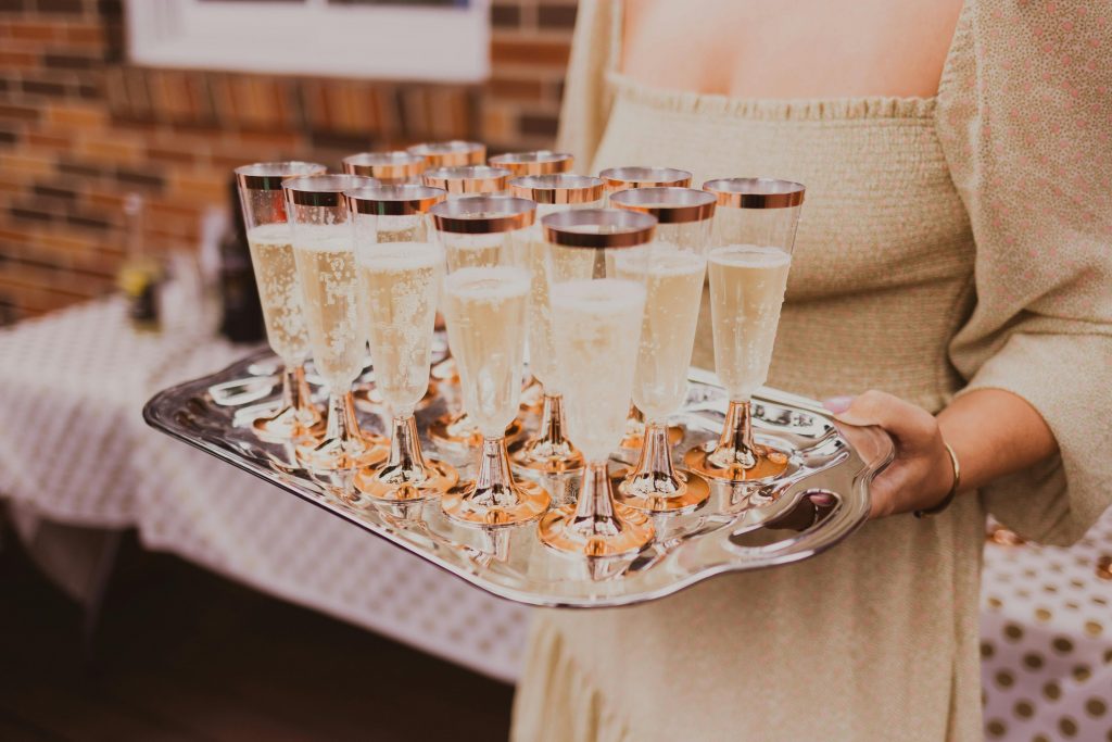 pexels-photo-5306739-5306739 A tray of champagne flutes carried by a woman at an elegant indoor party.